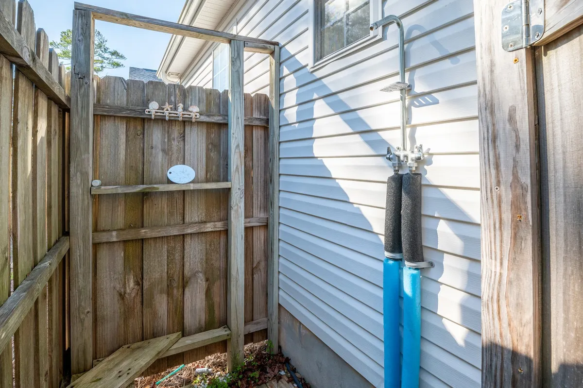 This image features the private outdoor shower with a wooden fence and water hose, a refreshing retreat after a day at the beach. The scene is simple yet functional, emphasizing convenience and beachside living.