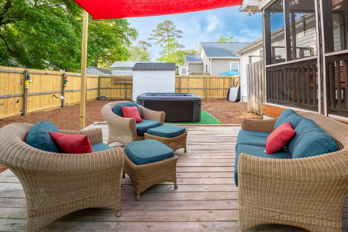 A comfortable outdoor living area featuring cushioned wicker seating, a hot tub sheltered under a vibrant red canopy, and ample space for relaxing or entertaining. The setting is designed for group gatherings, with views of the sunset and a cozy ambiance for both day and night enjoyment.