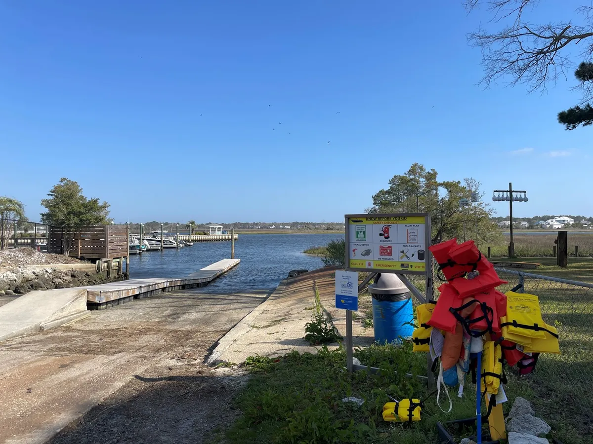 The image showcases a dock extending over a calm waterway, equipped with life jackets and an information sign. The serene setting is ideal for launching kayaks, paddleboards, or enjoying social gatherings by the water.