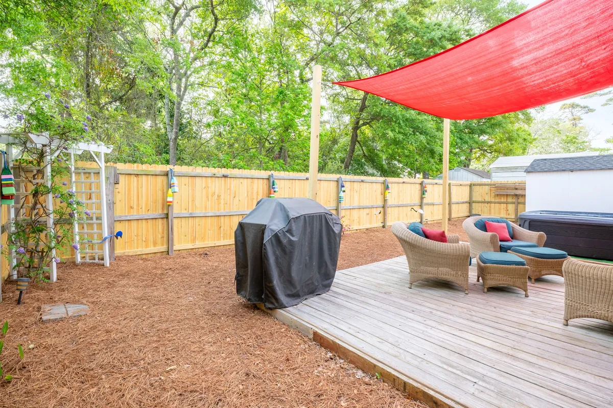 A welcoming outdoor space with a gas grill and ample seating beneath a red shade sail, enclosed by a fenced area. The setup is ideal for barbecues, outdoor dining, and socializing, capturing the essence of memorable group cookouts.