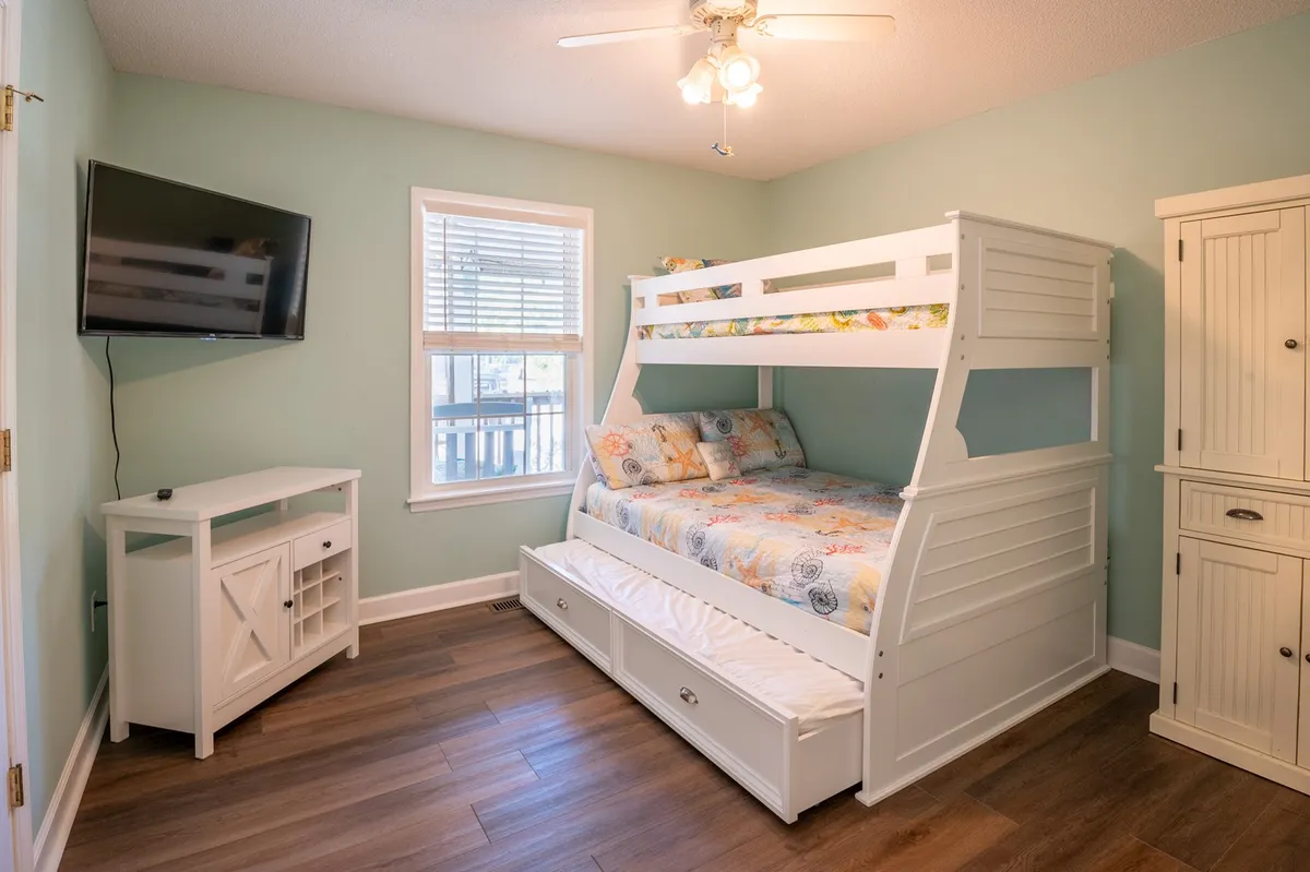 A cheerful bunk room with a sturdy bunk bed, a TV for entertainment, and a large window letting in daylight. The space feels playful and inviting, perfect for children or extra guests.