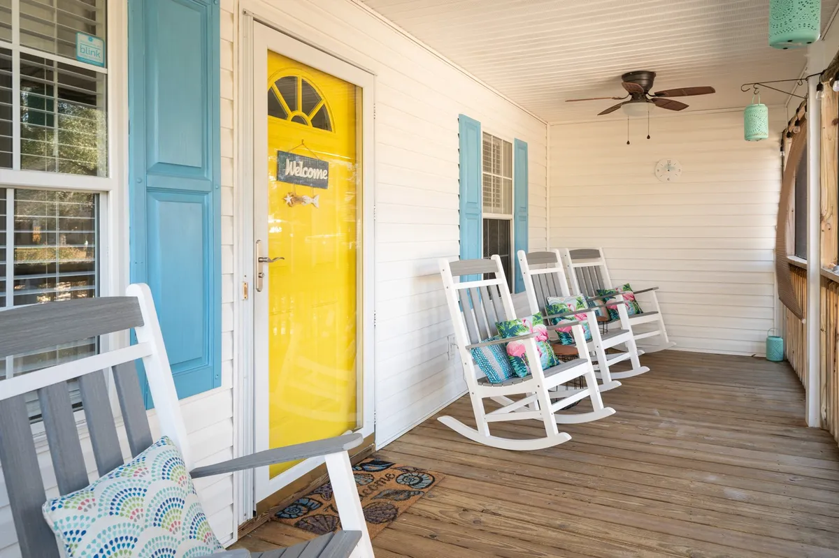 Showcasing the inviting front porch with bright yellow door, two classic rocking chairs, decorative cushions, and ample natural light. This spot is perfect for enjoying a quiet morning coffee or unwinding with a book, as described in the section.