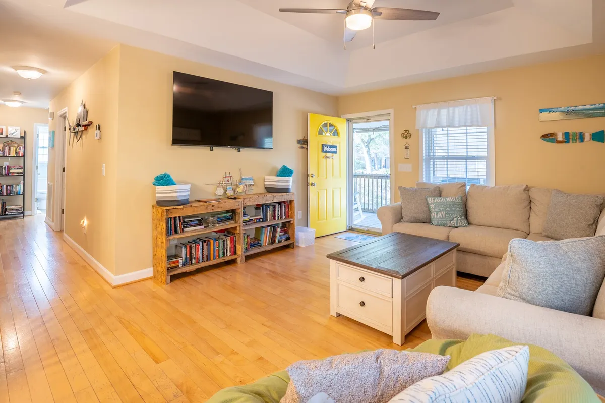 A sunny living area with a comfortable couch, wooden bookshelves lined with books, a coffee table, and a bright yellow door. The room exudes a relaxed, inviting mood, and offers both spaces for conversation and quiet reading.