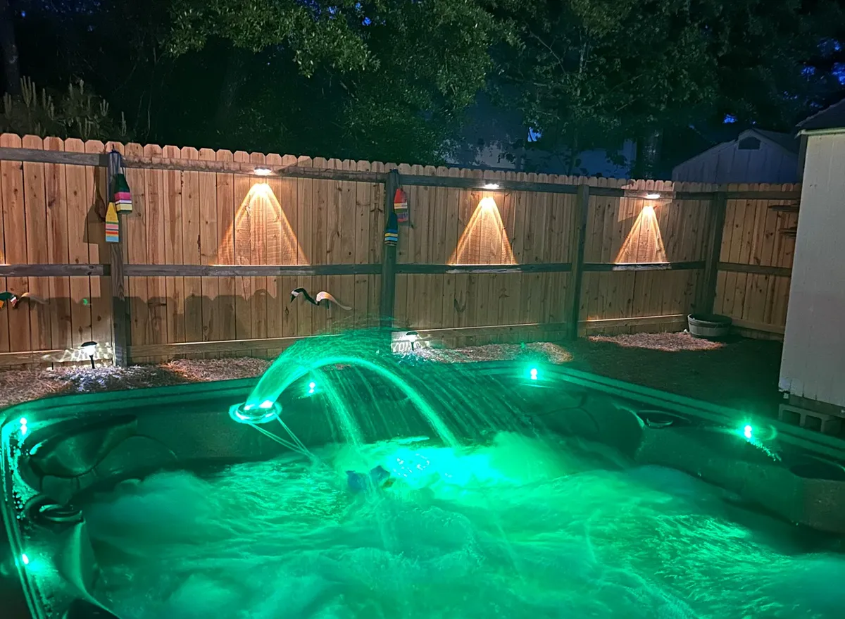 Set in a tranquil backyard, this image features a hot tub with water features and soft lighting on the fence. The mood is intimate, suggesting relaxation after an adventurous day outdoors—ideal for stargazing or evening socializing.