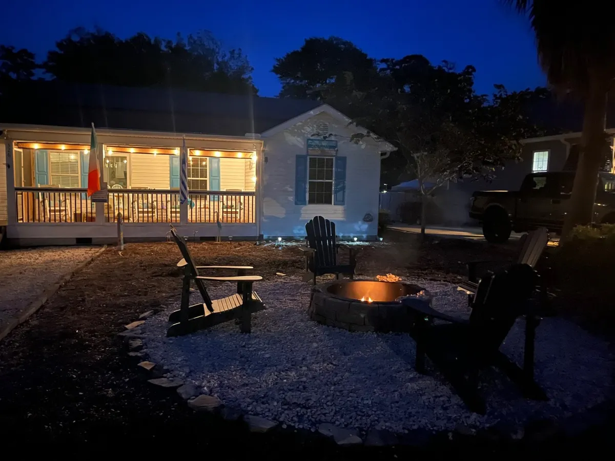 An inviting fire pit sits surrounded by Adirondack chairs in a well-lit yard in front of the house. The space is designed for gatherings, with warm outdoor lighting creating a cozy, communal ambiance perfect for unwinding after a day of play.