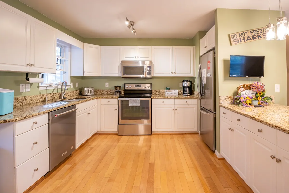 This image captures a welcoming kitchen scene with granite countertops, stainless steel appliances, a spacious kitchen island, and colorful decor accents. The layout is open and designed for gathering, with plenty of room for food preparation and socializing.