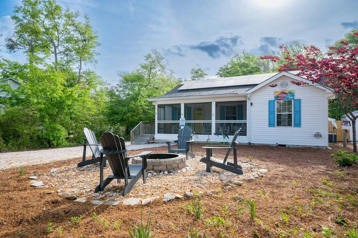This photo shows a cozy fire pit surrounded by Adirondack chairs, set in a landscaped yard with views of the house and solar panels. The atmosphere is welcoming, ideal for gathering with friends and family in the evenings or hosting outdoor barbecues.